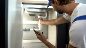 Professional plumber inspecting pipes under a sink for leaks in a home